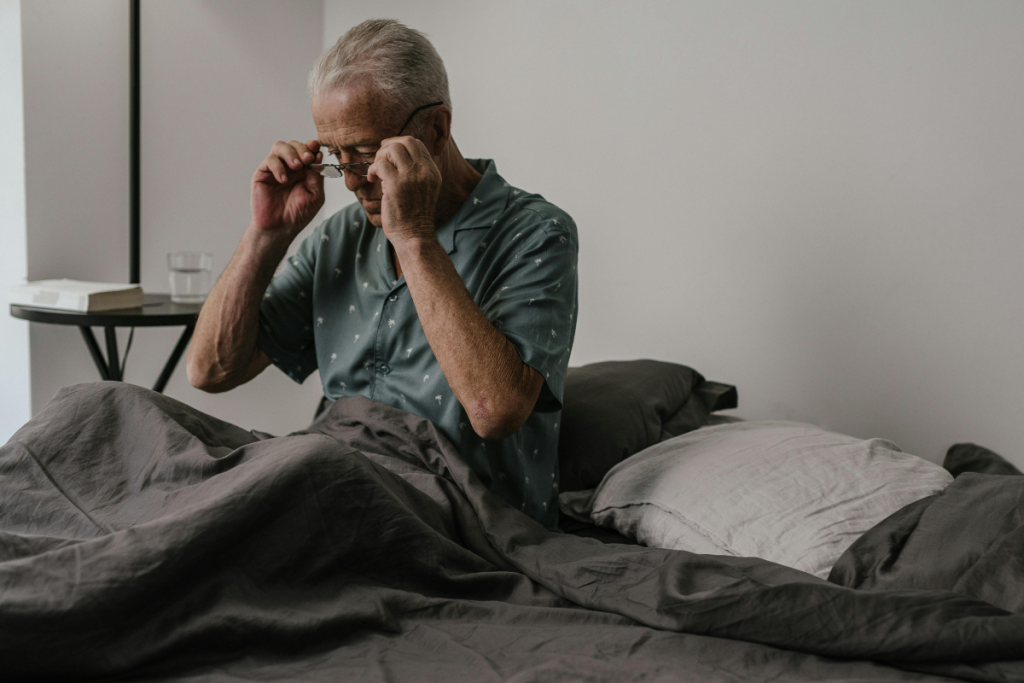 Una fotografia di un anziano a letto che si mette gli occhiali